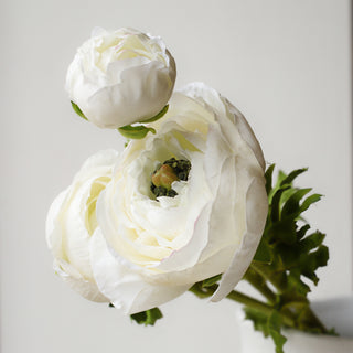 Close-up of a faux real touch white ranunculus bloom with layered petals and green centre