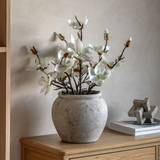 Faux magnolia arrangement with white blossoms in a textured cement pot on a wooden console table