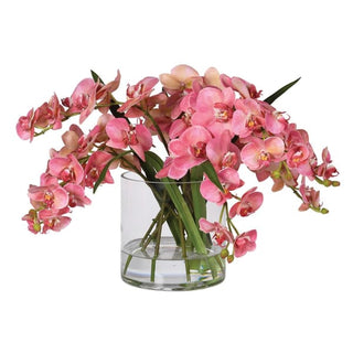 Faux pink Phalaenopsis orchid arrangement in a clear glass cylinder vase, showing the cascading rose-pink blooms with coral edges and yellow-red throat detail