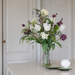 Faux tulip and artichoke floral arrangement in a clear glass vase with viburnum thistles and eucalyptus foliage