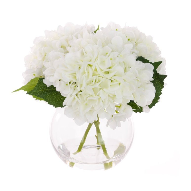 Faux white hydrangea arrangement in a clear globe glass vase with realistic stems and foliage