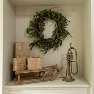 Decorative wreath, gift boxes, and a trumpet on a shelf with white cabinets.