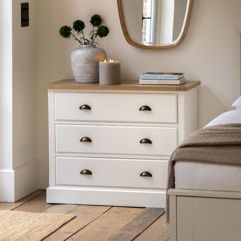 Florence 3 drawer chest of drawers in oak and white beside a bed with mirror and decor