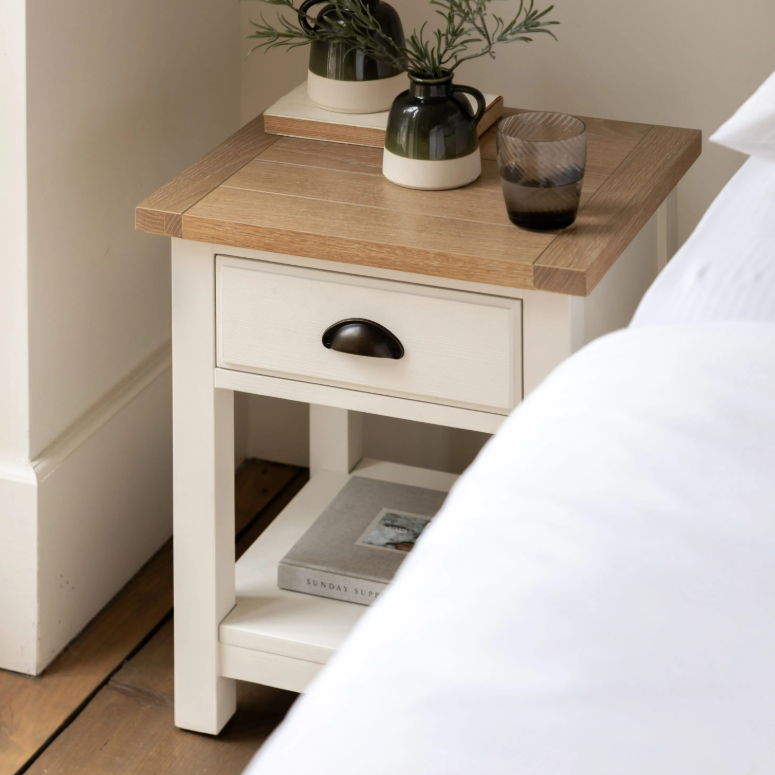 Florence bedside table in oak and white with drawer and open shelf beside a bed