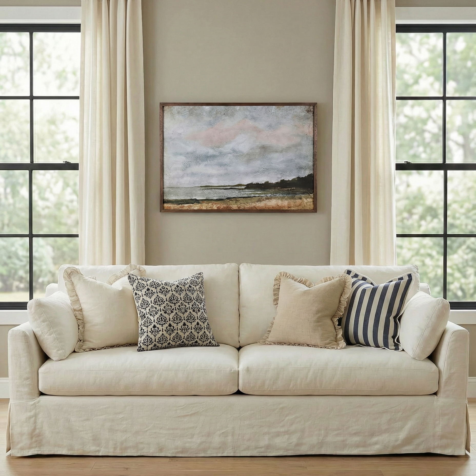 White sofa with decorative pillows in a living room setting with large windows and a painting on the wall.