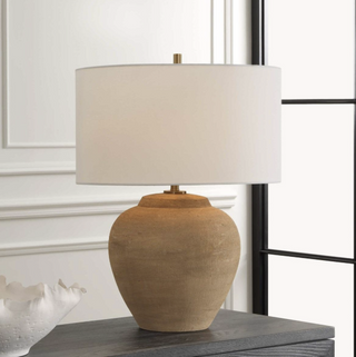 terracotta table lamp on a dark wood console, with a vase-form clay base and white linen drum shade against a panelled wall