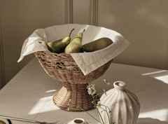 Handwoven natural rattan pedestal bowl styled with pears on a dining table