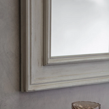 Close-up of a framed mirror with a wooden frame on a gray wall.
