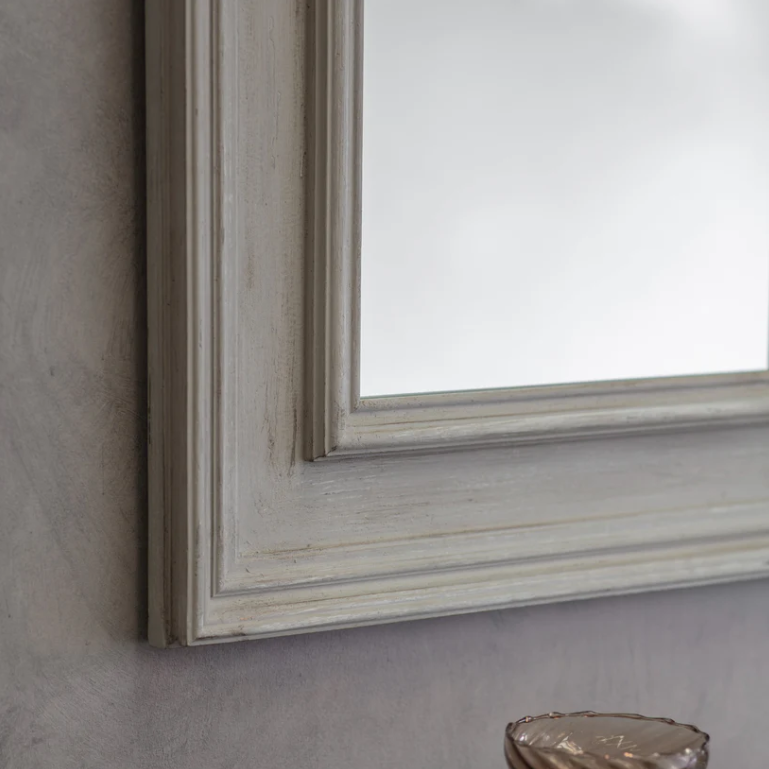 Close-up of a framed mirror with a wooden frame on a gray wall.