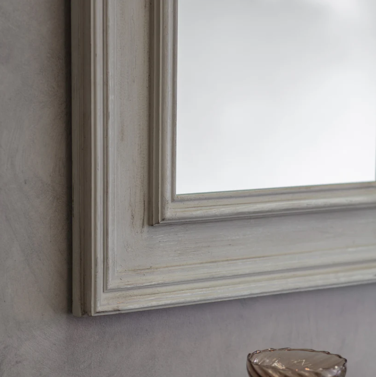 Close-up of a framed mirror with a wooden frame on a gray wall.