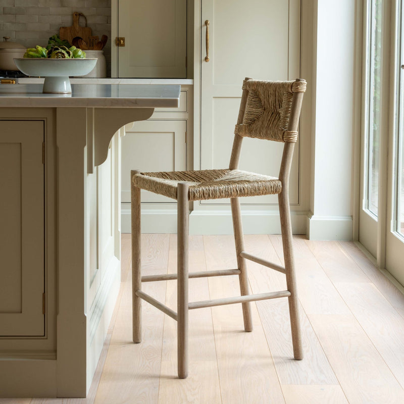 Wooden bar stool in a kitchen setting with light wood flooring and neutral color palette.