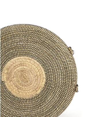 A close-up of a woven round basket or tray made from natural straw and raffia, showing a textured dark brown outer weave and a lighter tan circular inset, photographed on a plain white background.