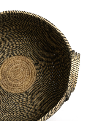 Close-up of a woven basket viewed from above, showing a dark brown to black exterior and a natural tan straw interior with a circular woven base, on a white background.
