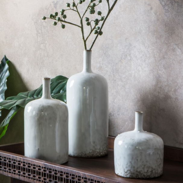 Set of three white ceramic vases with soft white glaze and textured bases styled on wooden console
