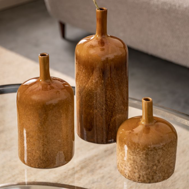 Three brown ceramic vases on a reflective surface with a blurred background