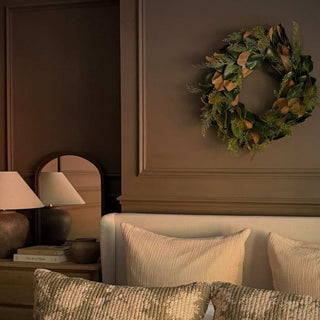 Faux magnolia wreath hung above a bed against a dark panelled wall