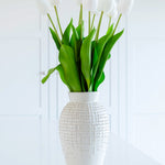 A stunning white ceramic vase holding white lilies. There is a raised-bump pattern on the exterior of the vase