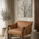 Brown leather armchair in a living room with a tree painting on the wall.