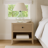 Open shelf oak bedside in front of bedroom window with glass lamp and ceramic bowl