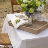 Outdoor table setting with flowers, glasses, and a napkin on a white tablecloth.