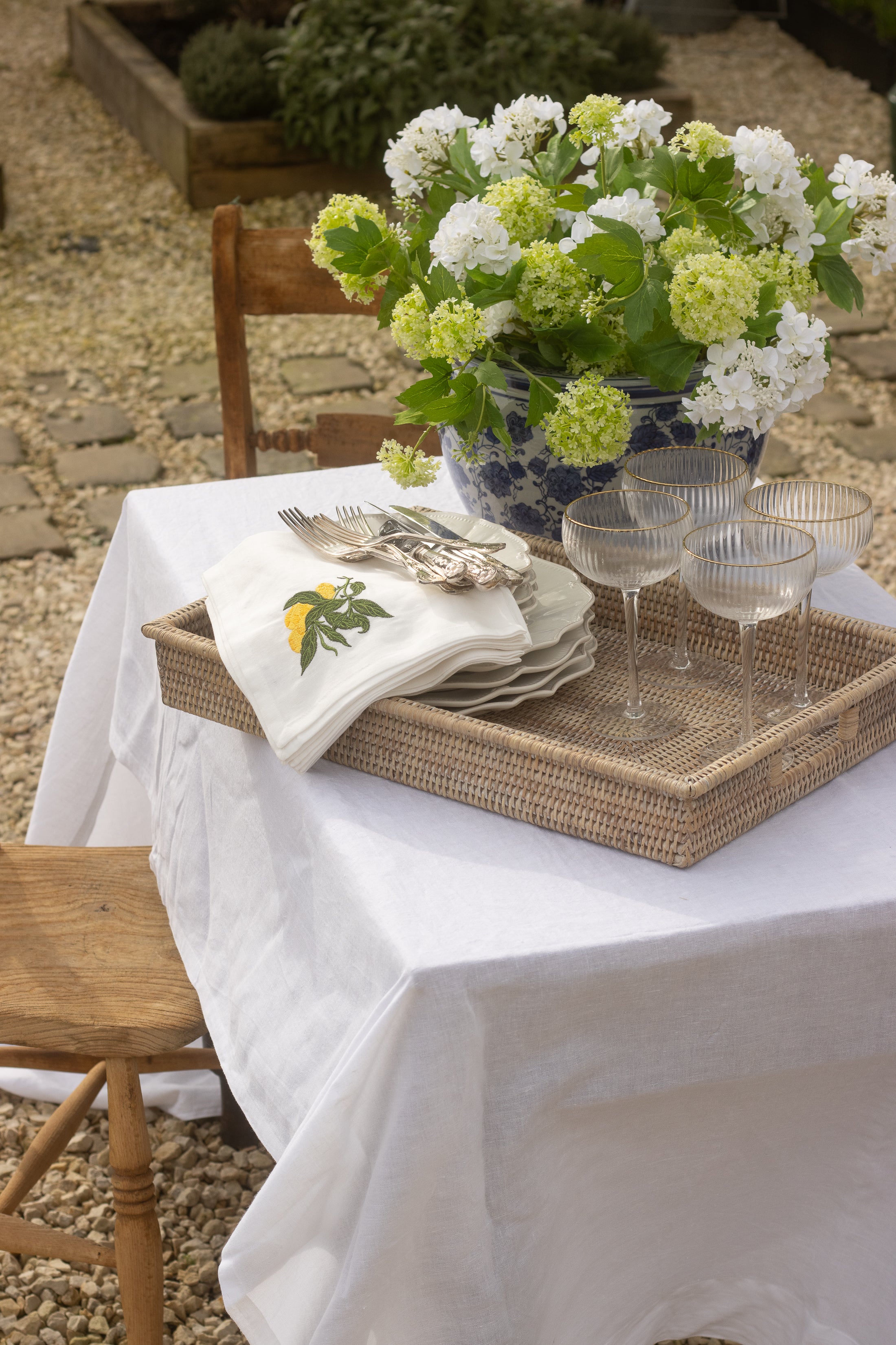 Outdoor table setting with flowers, glasses, and a napkin on a white tablecloth.