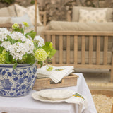Outdoor setting with a table set for a meal, featuring a blue and white floral pot and greenery.