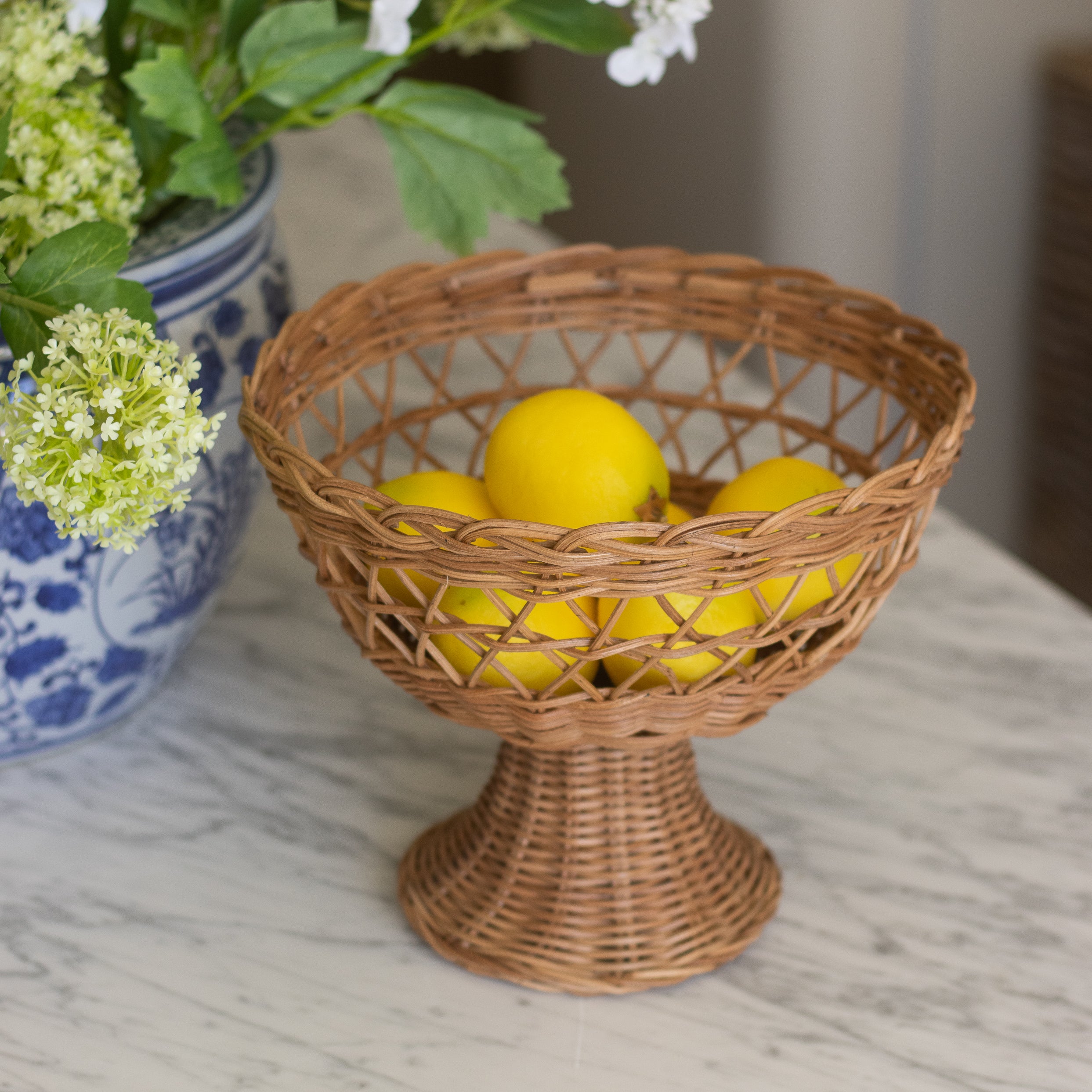 Wicker bowl with lemons on a marble surface next to a vase with flowers.
