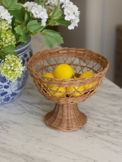 Wicker bowl with lemons on a marble surface next to a vase with flowers.