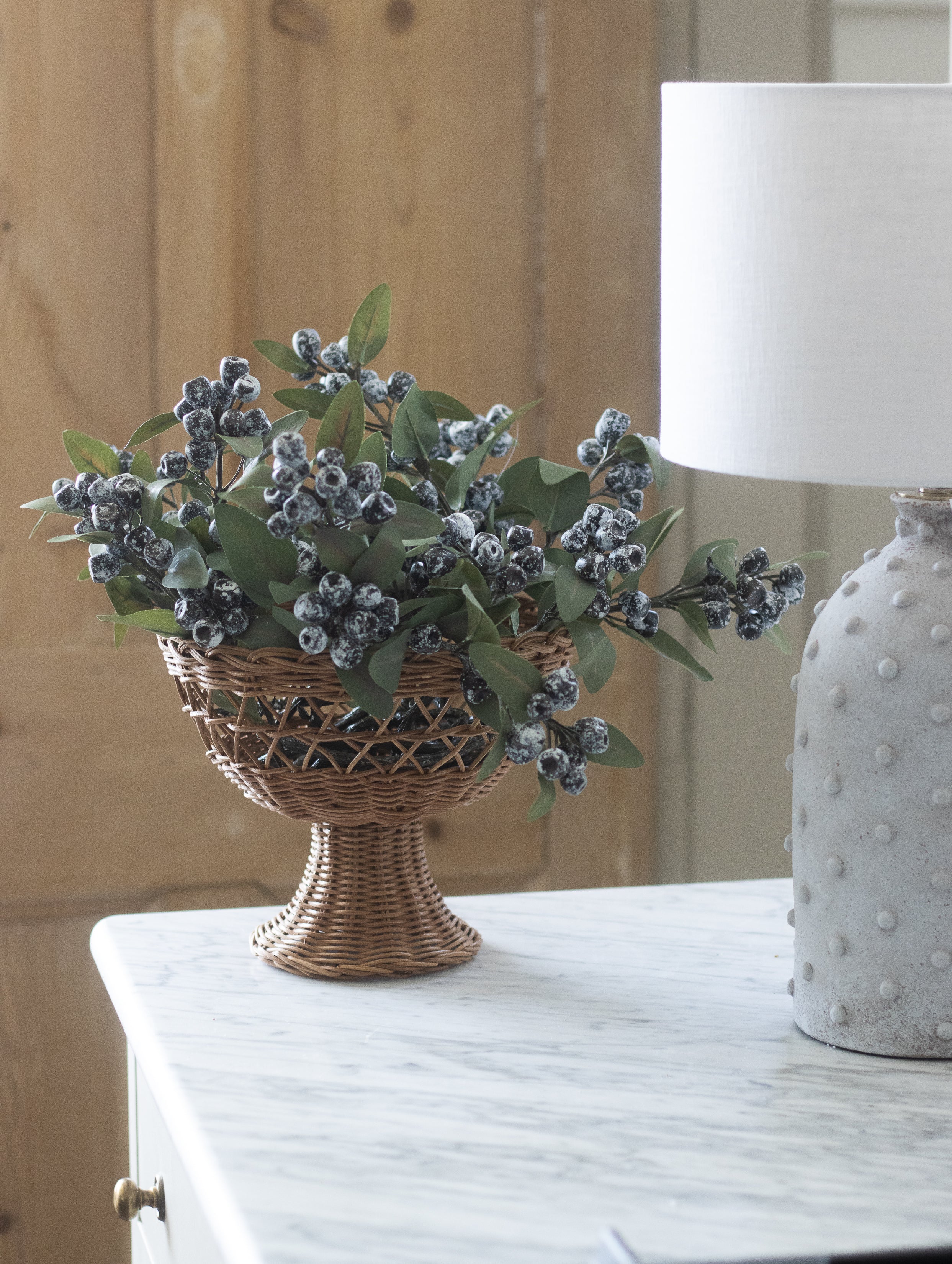 Decorative plant in a woven basket on a wooden surface with a lamp in the background.