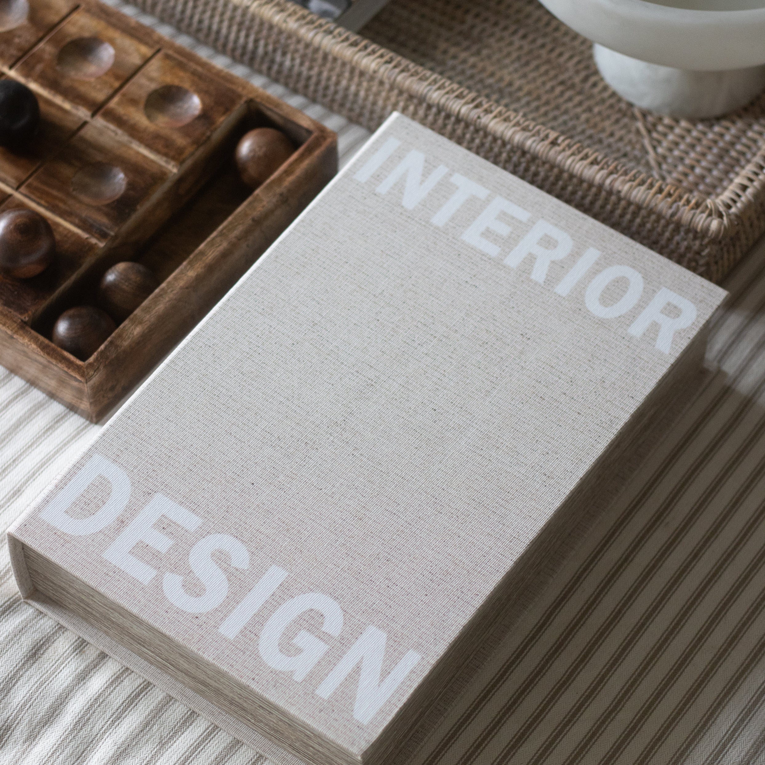Book titled 'Interior Design' on a surface with a wooden box and white bowl in the background.