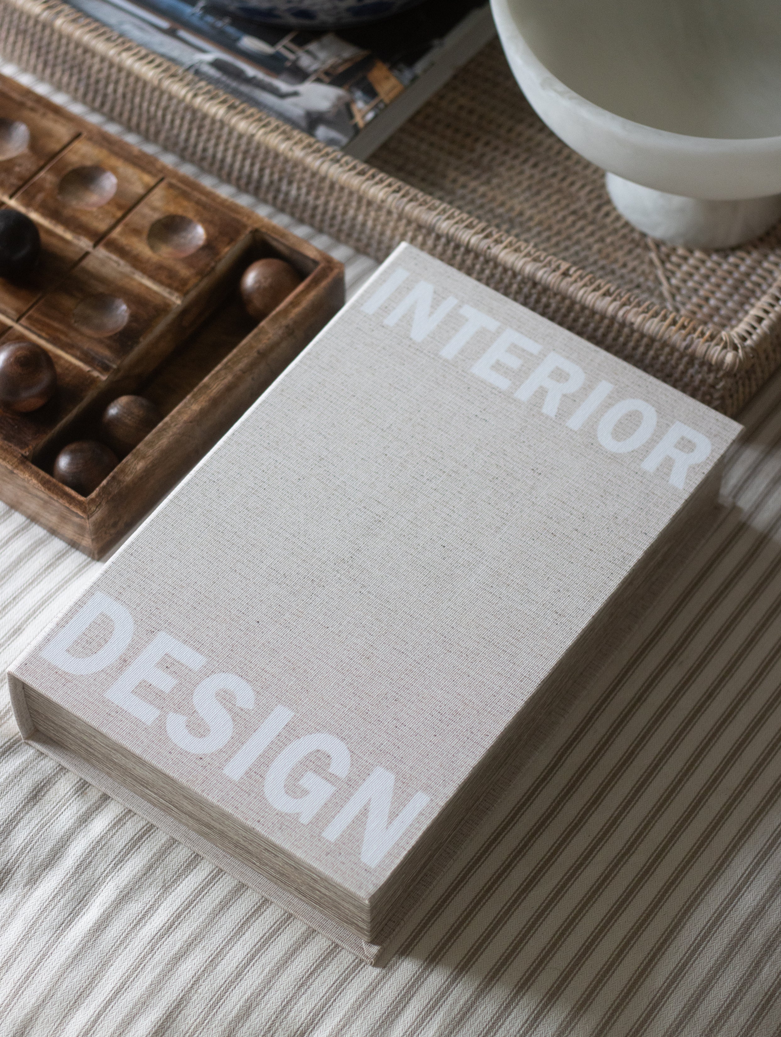 Book titled 'Interior Design' on a surface with a wooden box and white bowl in the background.