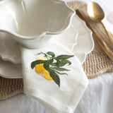 White ceramic bowl with embroidered lemon and leaf design on a white tablecloth.