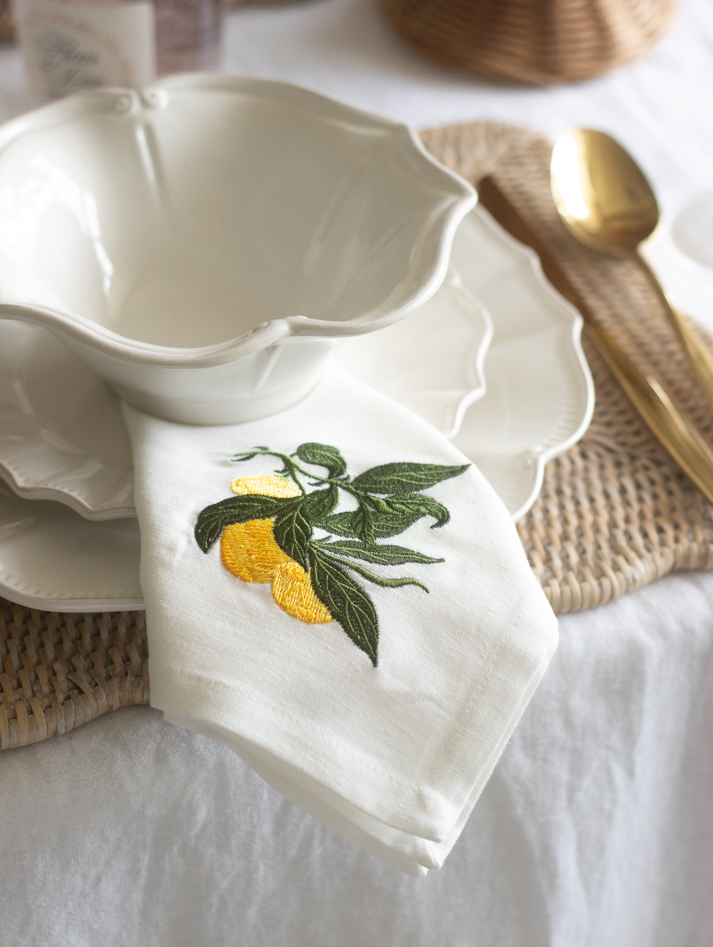 White ceramic bowl with embroidered lemon and leaf design on a white tablecloth.