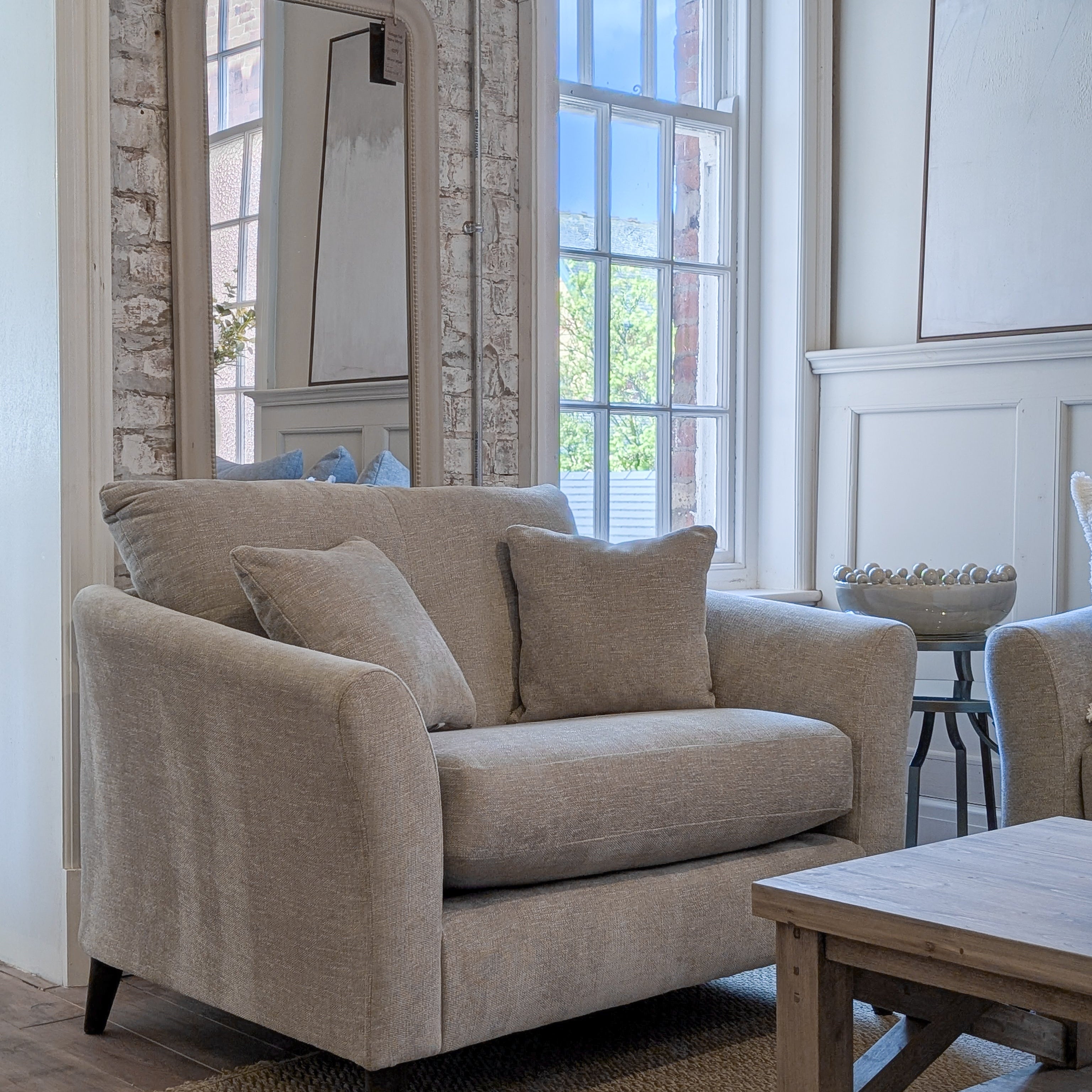 Beige sofa in a room with large windows and a brick wall.