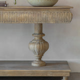 Wooden console table with decorative pedestal base against a plain wall