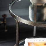 Jenner bronze glass side table with two tier round glass shelves beside a sofa in a modern interior
