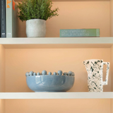 Decorative shelves with books, a plant, a light blue bobble bowl, a pitcher, and a woven basket.