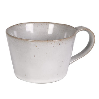 Single Lulworth stoneware cup with curved handle, showing the wide low café-style form, reactive cream glaze and russet rim banding