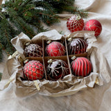 Set of six red glass Christmas baubles with silver detailing in a decorative storage box.