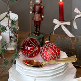 Decorative setting with red ornaments, nutcracker figurine, and lit candle on a wooden table.
