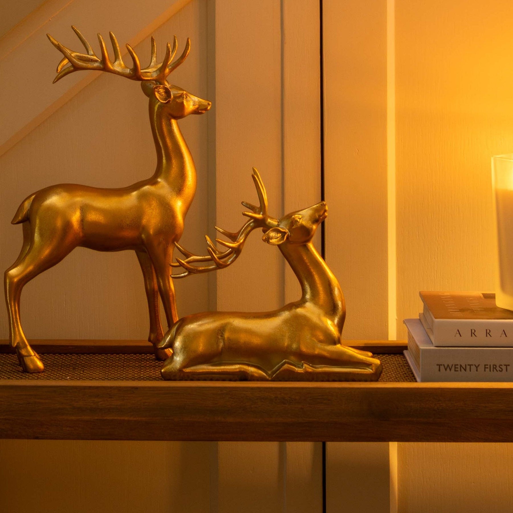 Gold deer figurines on a table with a candle and mirror in a warm-lit room.