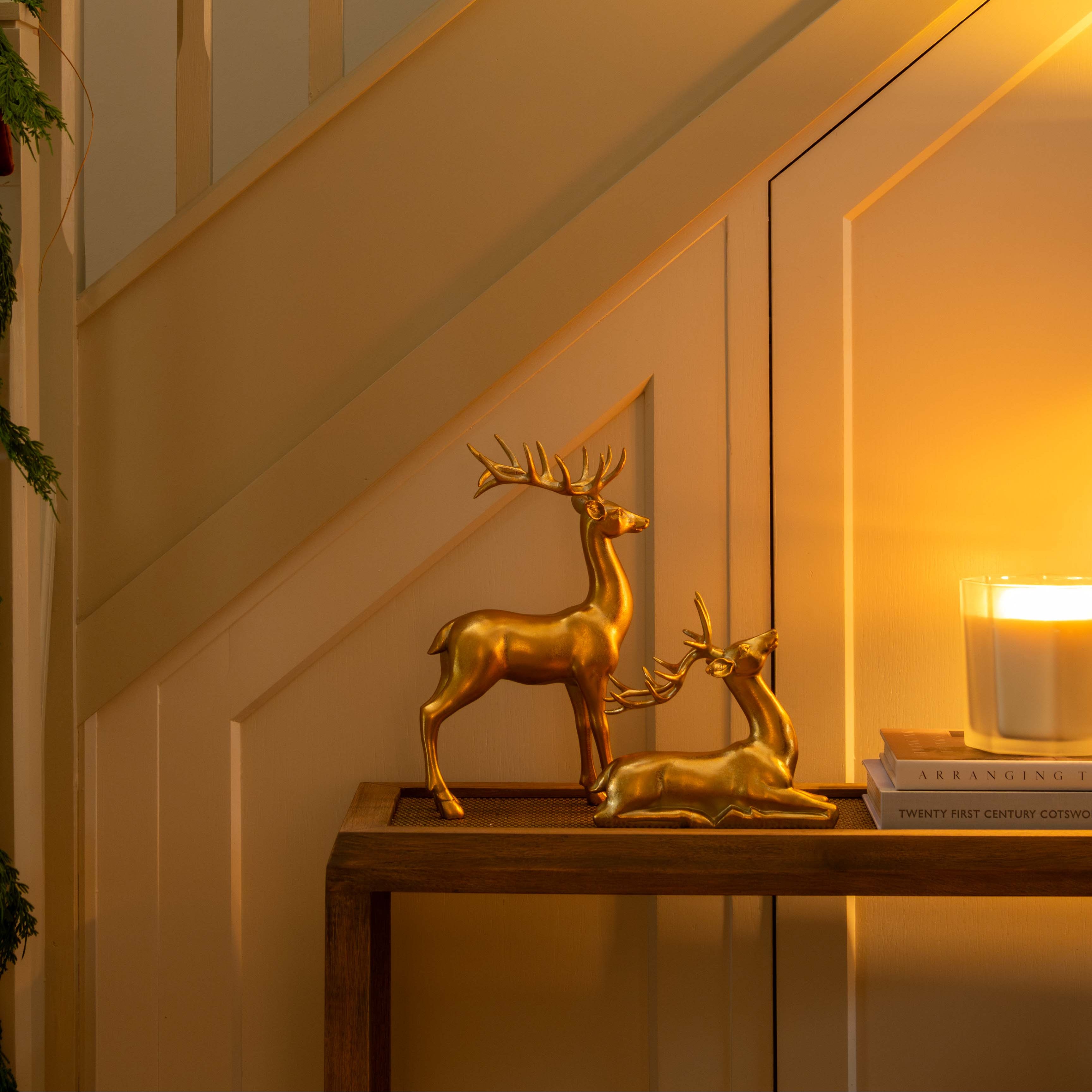 Gold deer figurines on a table with a candle and mirror in a warm-lit room.