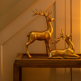 Gold deer figurines on a table with a candle and mirror in a warm-lit room.