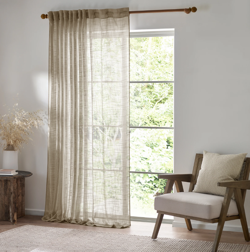 Living room with a large window, beige curtains, and a wooden chair with a cushion.
