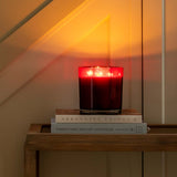 Red candle on a stack of books with a warm glow in a softly lit room.