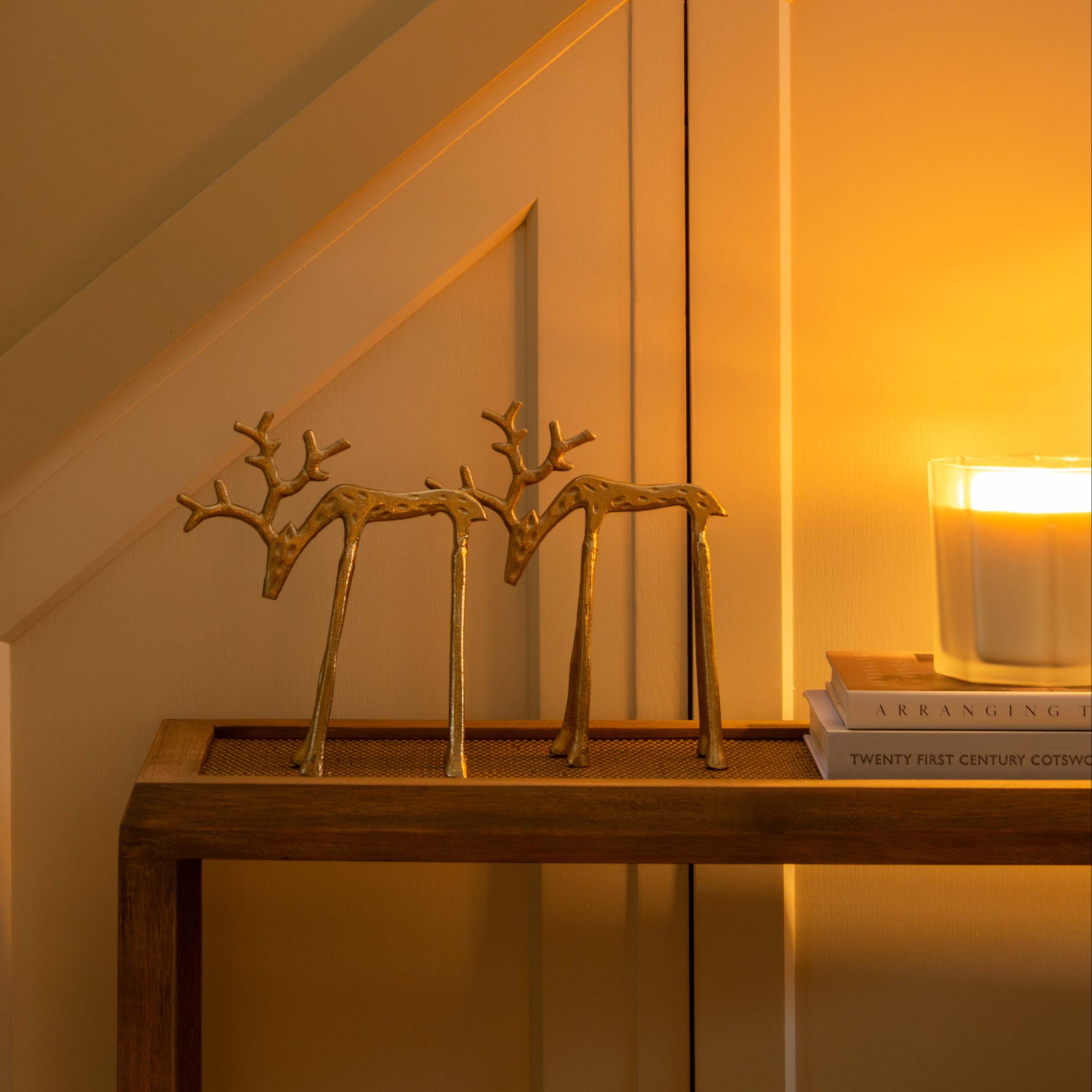 Decorative setup with gold reindeer sculptures and a candle on a table against a warm-toned wall.