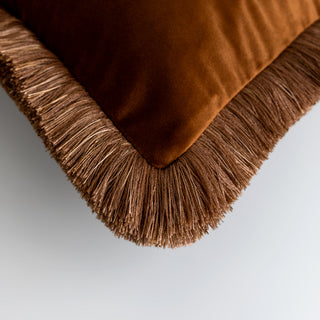 Naunton chestnut velvet rectangle cushion with fringe, styled on a sofa
