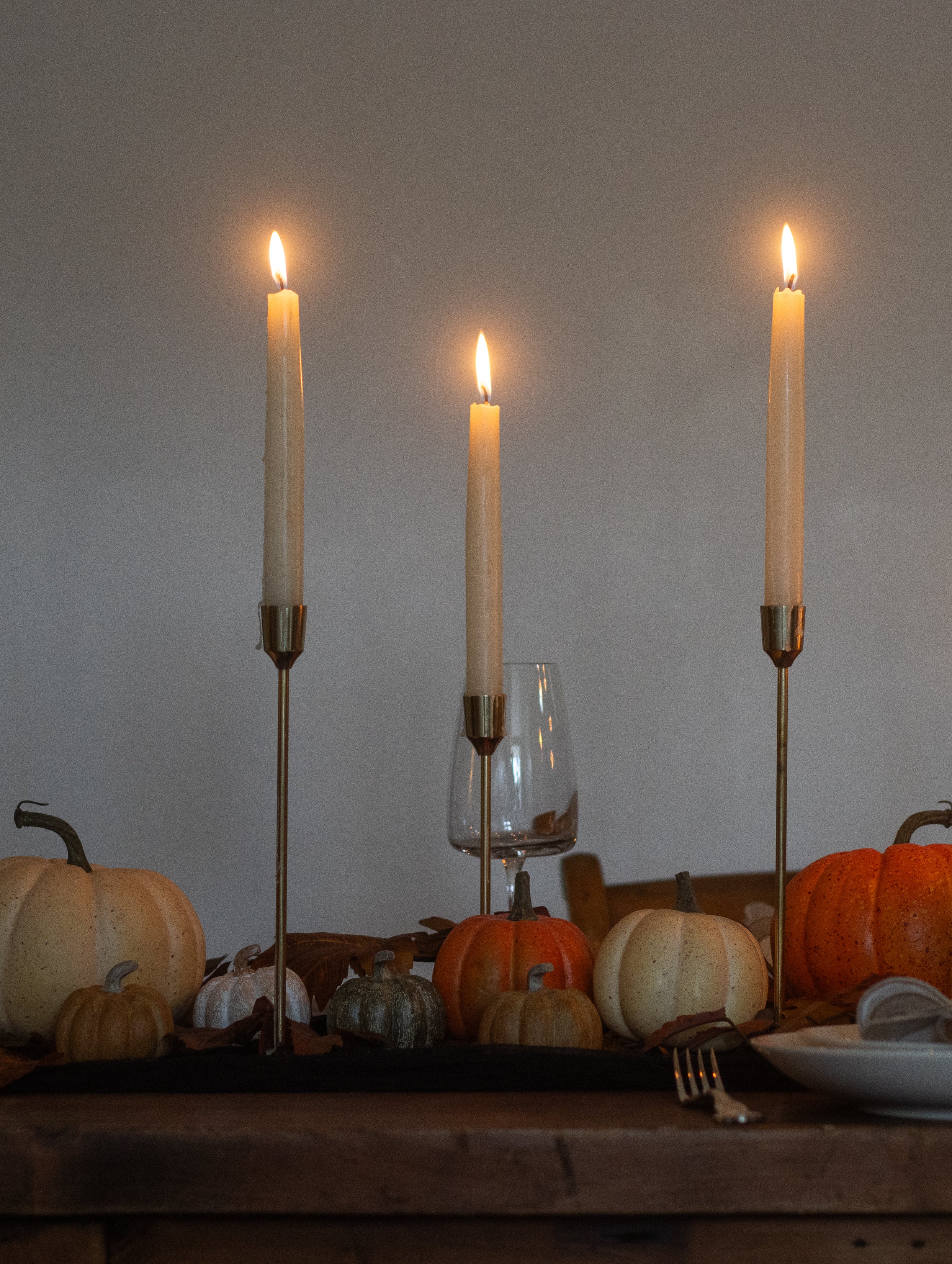 Table setting with candles, pumpkins, and a glass on a wooden surface.