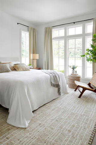 Neatly made bed in a bright bedroom with large windows and decorative elements.