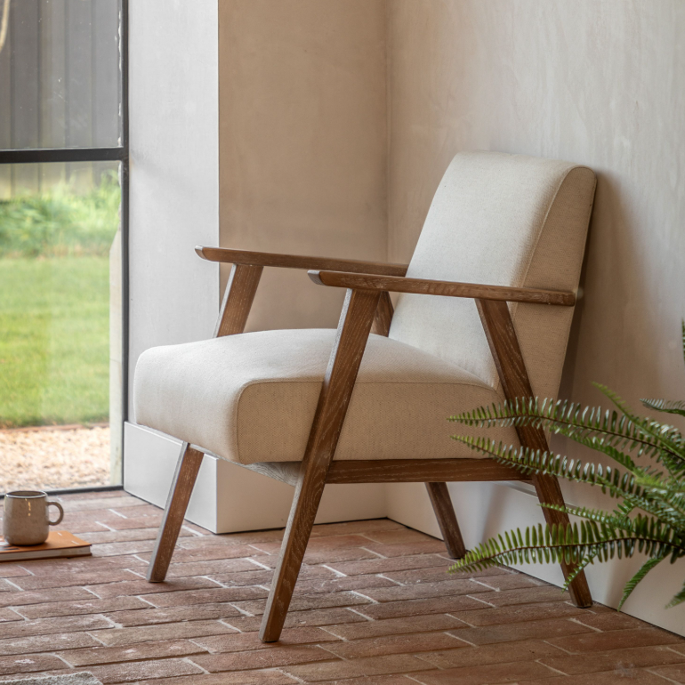 Beige armchair with wooden frame on a wooden floor next to a glass door.